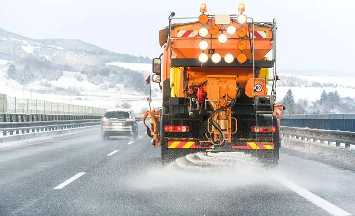 Snow plow on highway salting road. Orange truck deicing street.