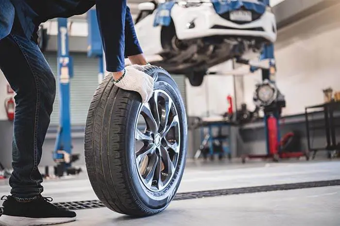 Male mechanic hold and rolling tire at repairing service garage